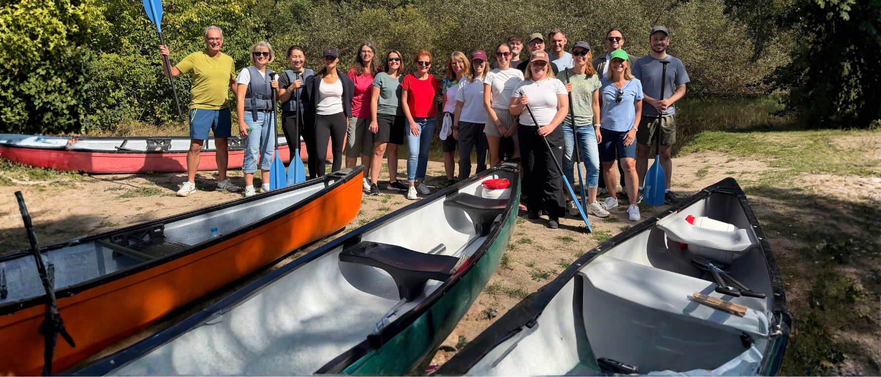 Das HR-Team von Heel steht bei seinem Kanu-Teamevent im Elsass mit Paddeln am Ufer der Moder