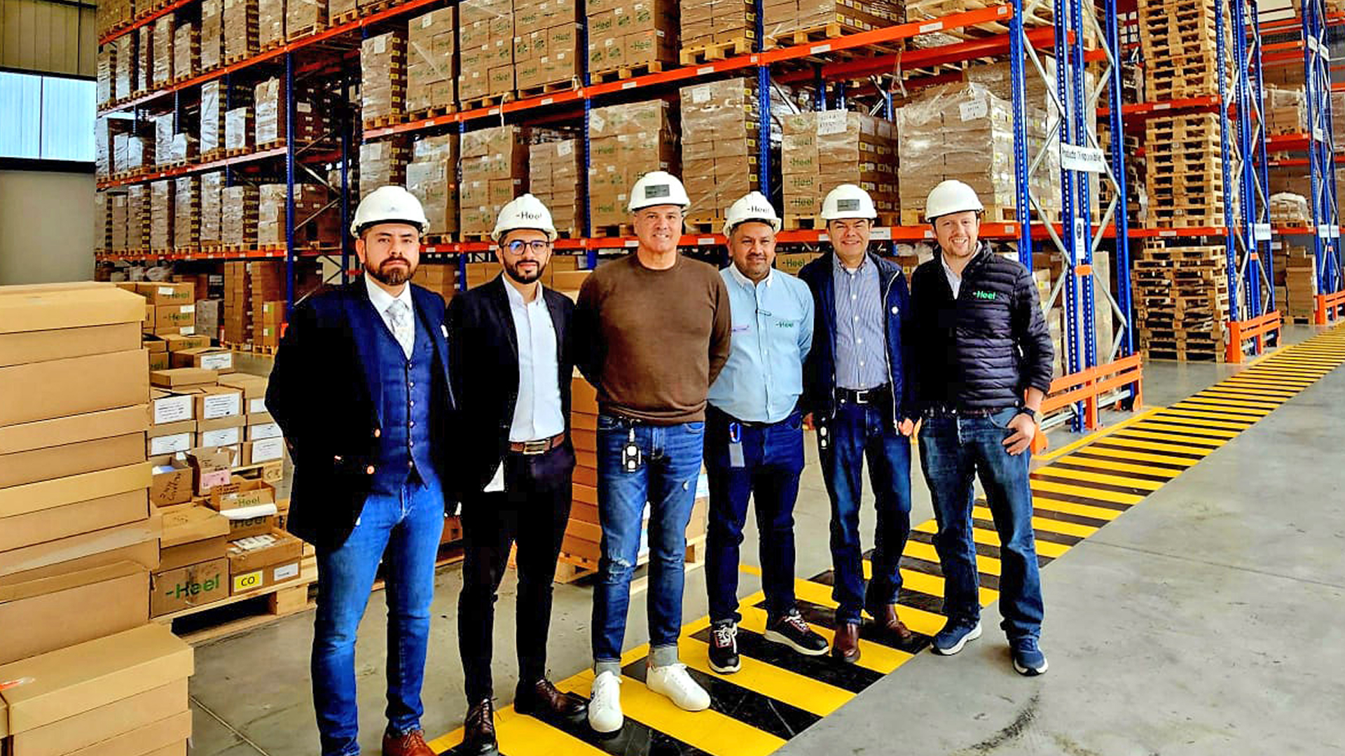 Heel Mitarbeiter stehen nebeneinander im neuen und modernen Distributionszentrum vor einem Hochregallager.